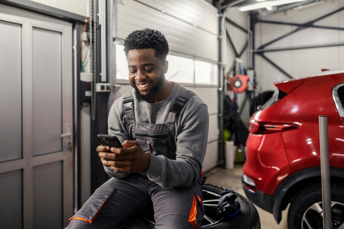 Car service worker sitting on a stack of tires while typing on a phone