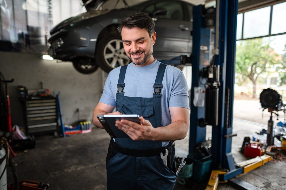 Mechanic with a digital tablet beside a car raised on a hydraulic lift
